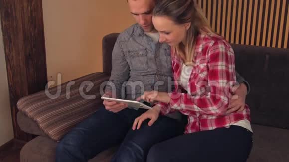 年轻快乐的一对夫妇坐在家里的沙发上用平板电脑看电影视频的预览图