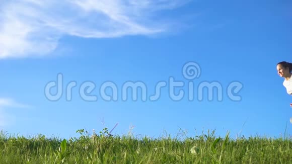 快乐的女孩在蓝天的绿色草地上奔跑视频的预览图