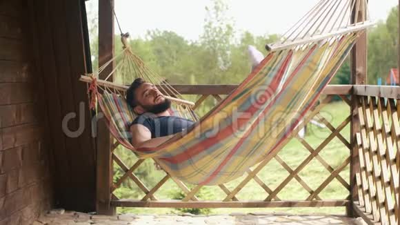 一个小胡子男人睡在乡下房子的吊床上他用平板电脑睡觉视频的预览图