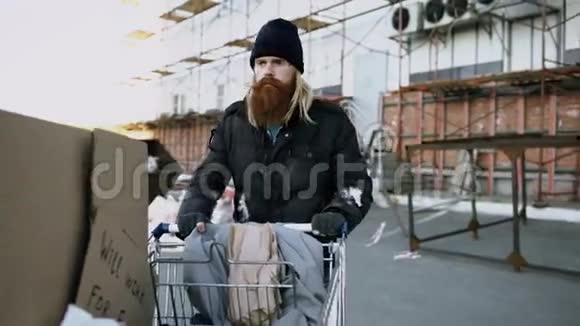在寒冷的秋日一个长着胡须的流浪汉拿着鞋牌在街上走着视频的预览图