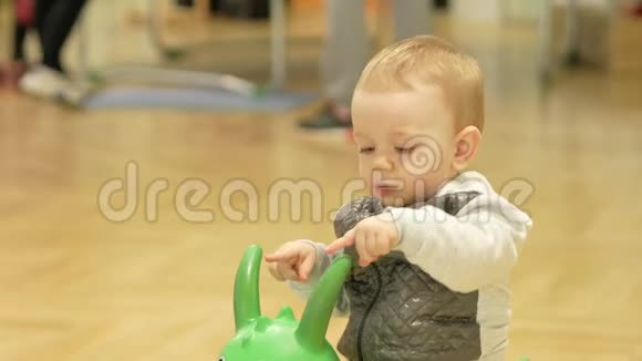 两岁可爱的金发男孩在商场里骑着一匹充气马跳跳孩子们在后台跑来跑去视频的预览图