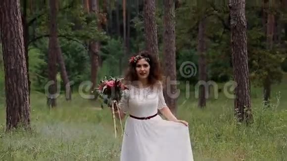 美丽的新娘穿着一件复古的裙子在夏天的森林里有彩色的花束走到镜头前微笑视频的预览图