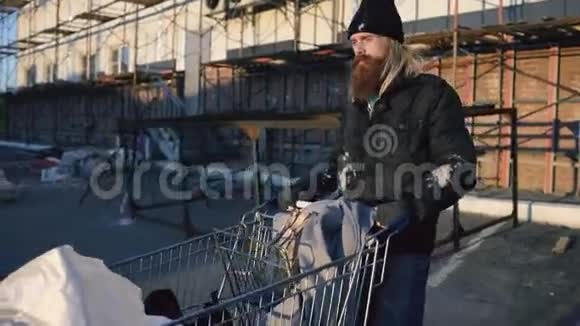 在寒冷的秋日一个长着胡须的流浪汉拿着鞋牌在街上走着视频的预览图