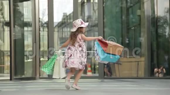 可爱的小女孩带着购物袋走出商店购物愉快视频的预览图