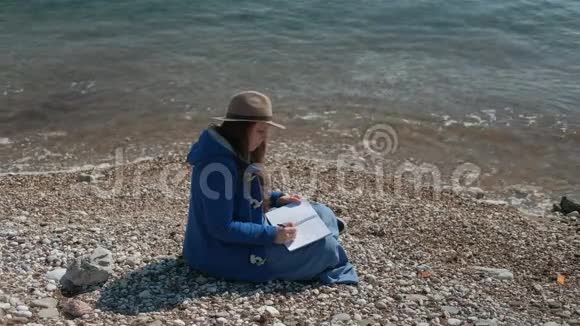 秋天的下午年轻的女人坐在河岸上写字视频的预览图
