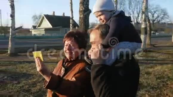 祖父和祖母带着孙子在公园里散步和他们的亲戚在公园里用手机交谈视频的预览图