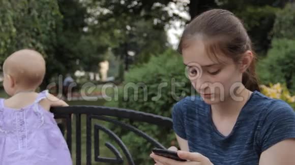 一个管理员在她的智能手机上按下按钮而小女孩则偷偷地离开了抱在长凳后面视频的预览图