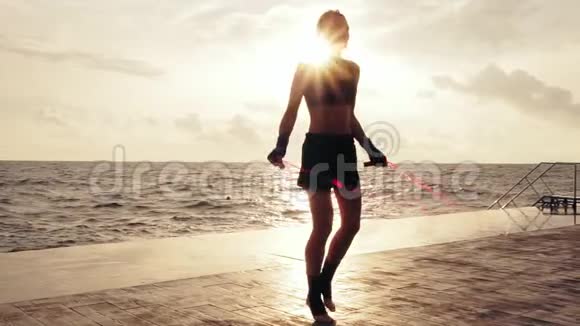 年轻女子在海滩边的阳光下慢慢地用跳绳一个跳跳绳的女孩视频的预览图