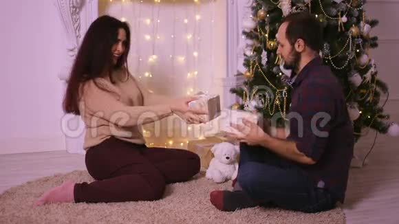 幸福的年轻夫妇坐在壁炉旁互相送礼物圣诞快乐视频的预览图