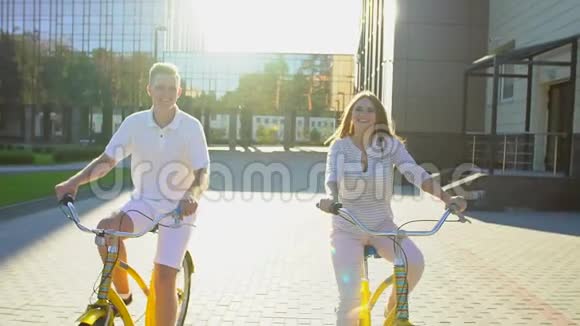 在夏天的户外一对年轻快乐浪漫的夫妇在阳光明媚的街道上快乐地骑自行车年轻人和女孩视频的预览图