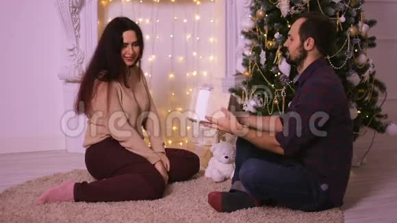 一个年轻人送他女朋友过圣诞节恋人们坐在米色地毯上的壁炉前视频的预览图