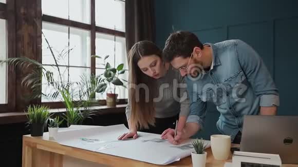 年轻的女人和男人是一个建筑师在办公室里工作蓝图笔记本电脑和房子模型视频的预览图