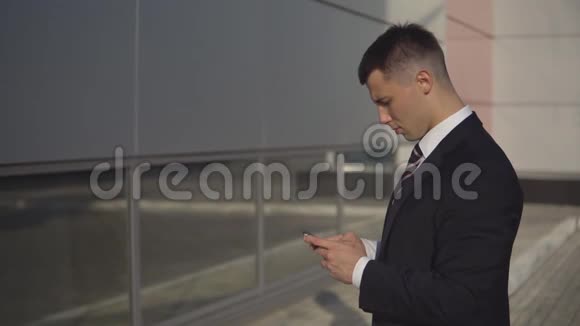 年轻的商人在智能手机上打字站在商业建筑户外的背景上视频的预览图