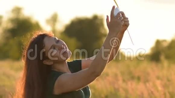 美丽的年轻女子在日落时在手机上拍了一张自我肖像在田野里微笑视频的预览图