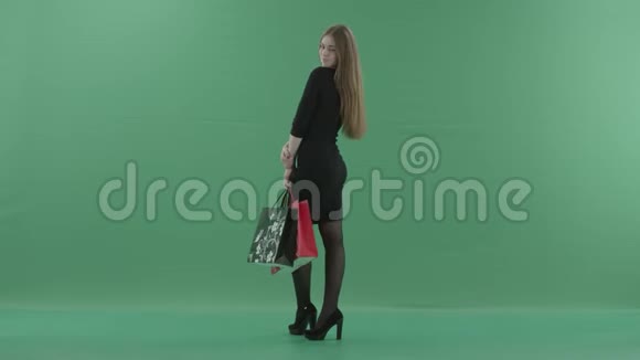 穿着黑色小礼服的美丽快乐的女人正拿着购物袋摆姿势她站在工作室里视频的预览图