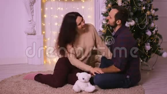 可爱的情侣坐在壁炉附近的地毯上女人和男人庆祝圣诞节视频的预览图