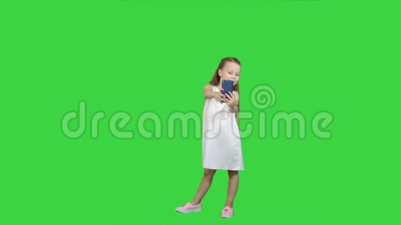 快乐的小女孩用绿色屏幕上的智能手机自拍色度键视频的预览图