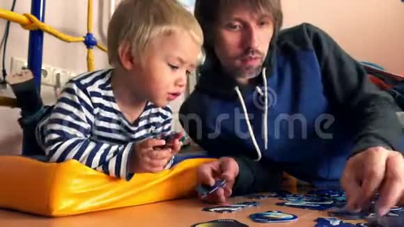 父亲和他的金发小儿子一起组装拼图男人和他的孩子在家里有空闲时间4K特写视频视频的预览图