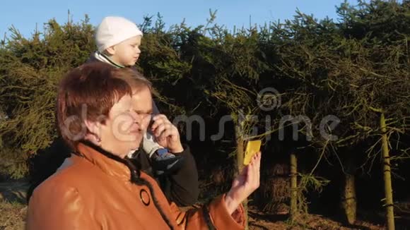 祖父和祖母带着孙子在公园里散步和他们的亲戚在公园里用手机交谈视频的预览图