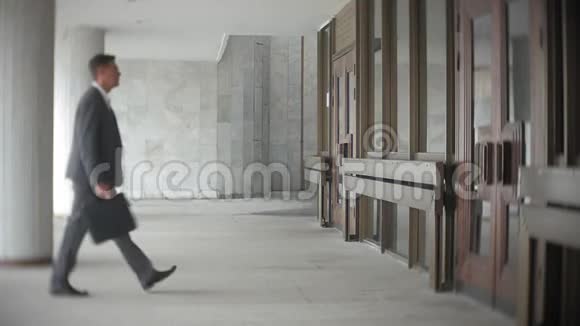 商人一边走一边提着公文包穿正装的男士在现代办公大楼附近散步视频的预览图