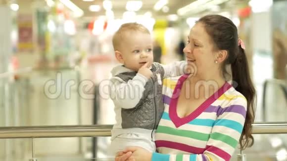 妈妈在商场里抱着一个漂亮的金发儿子在人们去购物的背景下视频的预览图