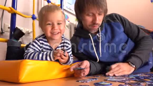 爸爸和他的小儿子一起在地板上组装拼图男人和他的孩子在家里有空闲时间4K视频视频的预览图