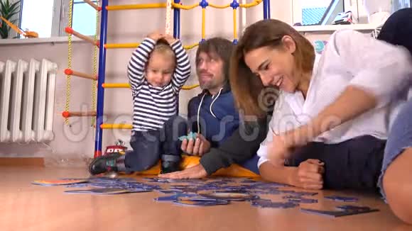 快乐的白种人家庭组装拼图男人女人和可爱的小男孩在一起有空闲时间4K视频的预览图