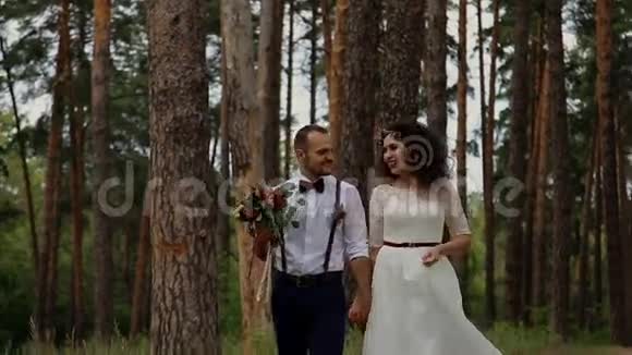 迷人的时尚新郎和他的新娘在豪华的松树林里散步相谈甚欢视频的预览图