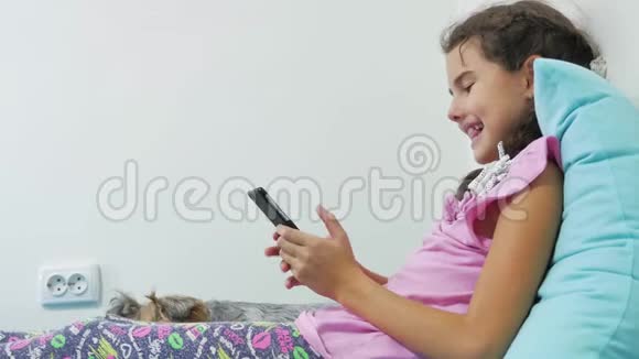 健康技术和美容理念带智能手机的小女孩在床上玩耍视频的预览图