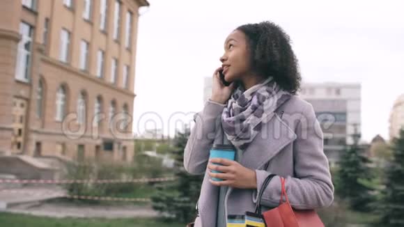 多莉拍摄了一个迷人的混合种族女孩谈论智能手机和喝咖啡步行在城市街道上的袋子青年视频的预览图