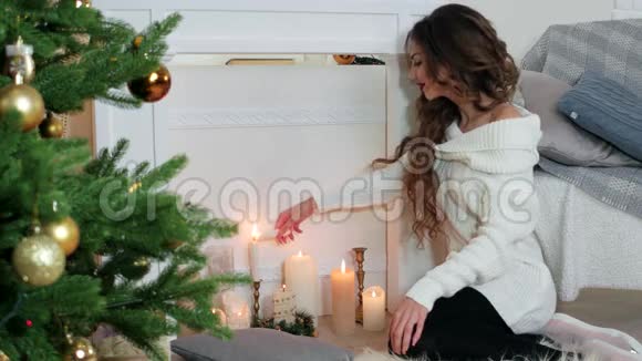 点燃蜡烛女孩许愿吹灭蜡烛坐在靠近圣诞树的壁炉旁视频的预览图