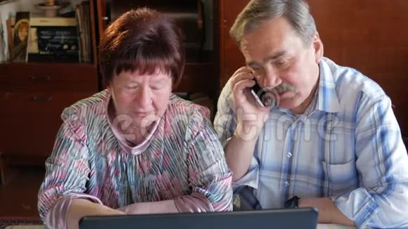 一对老夫妇坐在家里的笔记本电脑上女人看新闻男人用手机说话视频的预览图