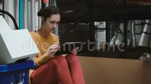 年轻女子坐在仓库里用平板电脑检查货物清单4K视频的预览图