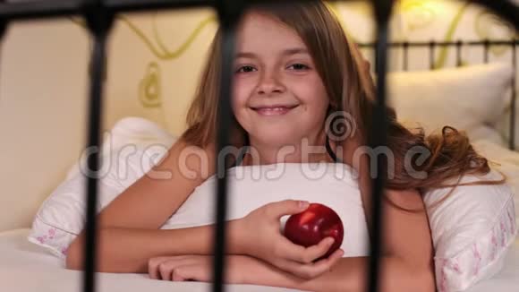 微笑着快乐的女孩在床上吃苹果视频的预览图