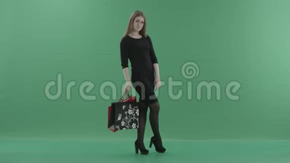 穿着黑色小礼服的美丽快乐的女人正拿着购物袋摆姿势她站在工作室里视频的预览图