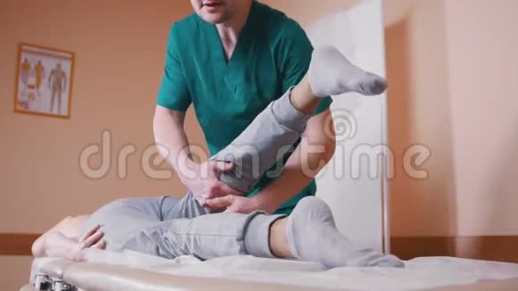 手动治疗师按摩躺在按摩台上的年轻女子伸展和弯曲她的髋关节视频的预览图