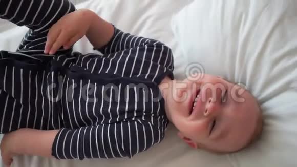 快乐的婴儿躺在床上慢慢地躺在白色床单上视频的预览图