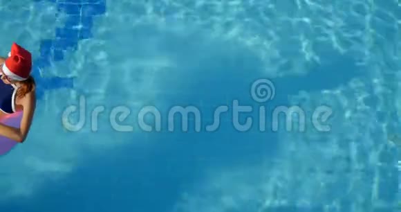 戴圣诞帽的女人在粉红色充气戒指上的游泳池里放松视频的预览图