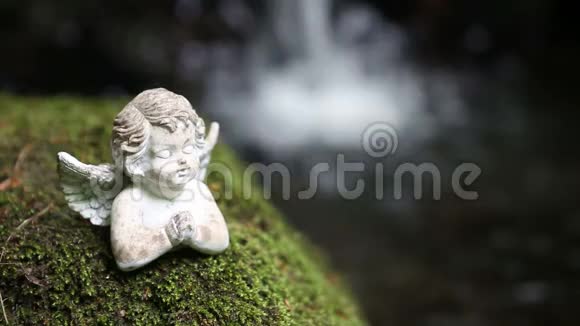 在瀑布前的苔藓上祈祷石头天使视频的预览图