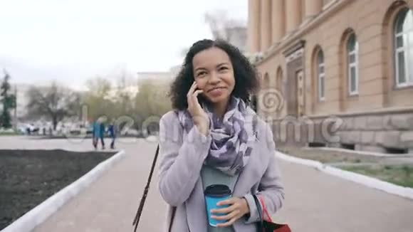 多莉拍摄的迷人的混合种族女孩交谈智能手机和喝咖啡步行在城市街道与袋青年视频的预览图
