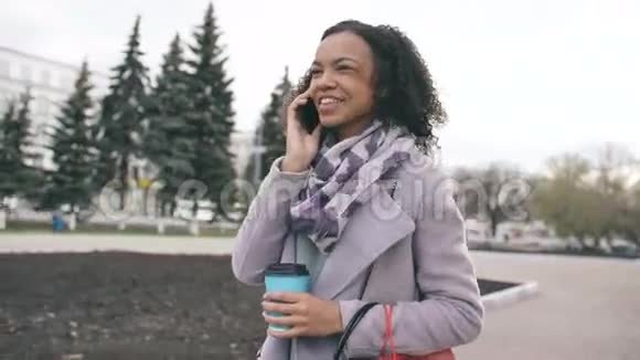 多莉拍摄的迷人的混合种族女孩交谈智能手机和喝咖啡步行在城市街道与袋青年视频的预览图