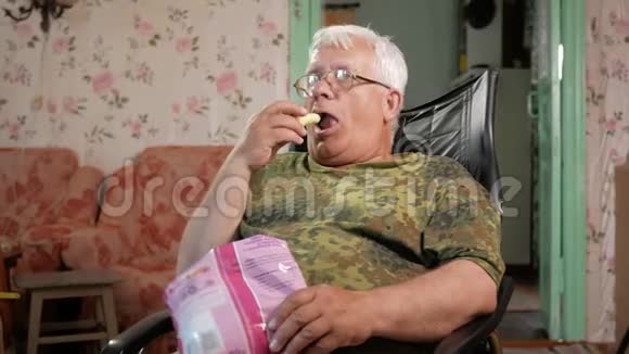 老人吃玉米棒看电视坐在带眼镜的皮扶手椅上视频的预览图