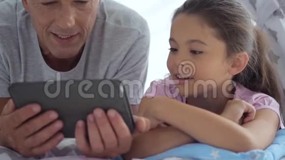 快乐的小女孩和她的父亲在家里用平板电脑视频的预览图