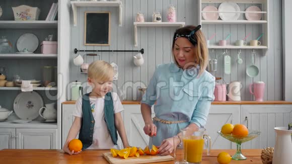 漂亮的妈妈靠近桌子她的孩子在厨房橘子躺在桌子上一家人看着它视频的预览图