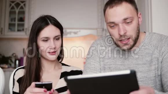 美丽的年轻夫妇男人和女人使用电话和平板电脑触摸屏在一个明亮的餐厅视频的预览图