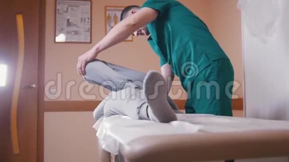 脊椎按摩师按摩躺在按摩台上的一名年轻女子伸展和弯曲她的髋关节压在膝盖上视频的预览图