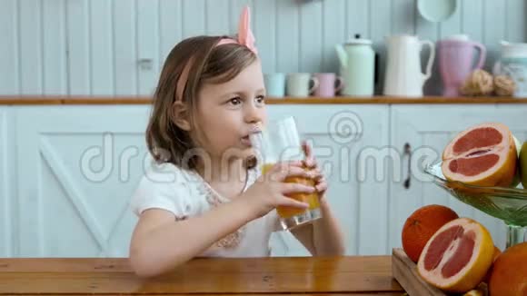可爱的小女孩早上在早餐时喝橙汁小孩子在桌上喝水果视频的预览图