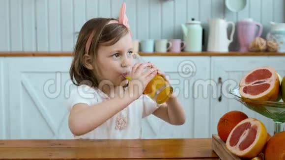 可爱的小女孩早上在早餐时喝橙汁小孩子在桌上喝水果视频的预览图