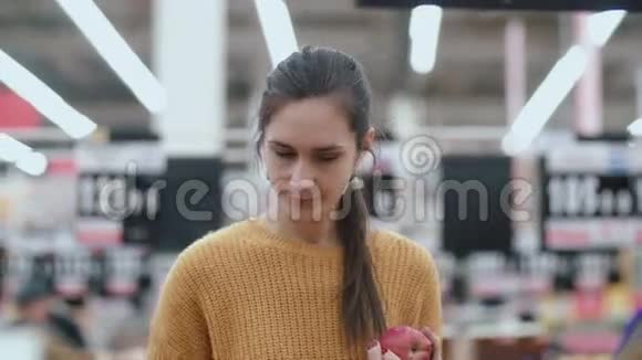 女人在超市里选择苹果的正面视图拿着苹果年轻女孩考虑水果4K视频的预览图