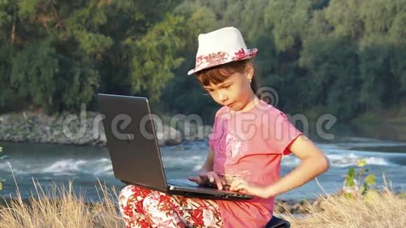 河岸上的女孩带着笔记本电脑一个小女孩拿着笔记本电脑在一条小河的岸边视频的预览图